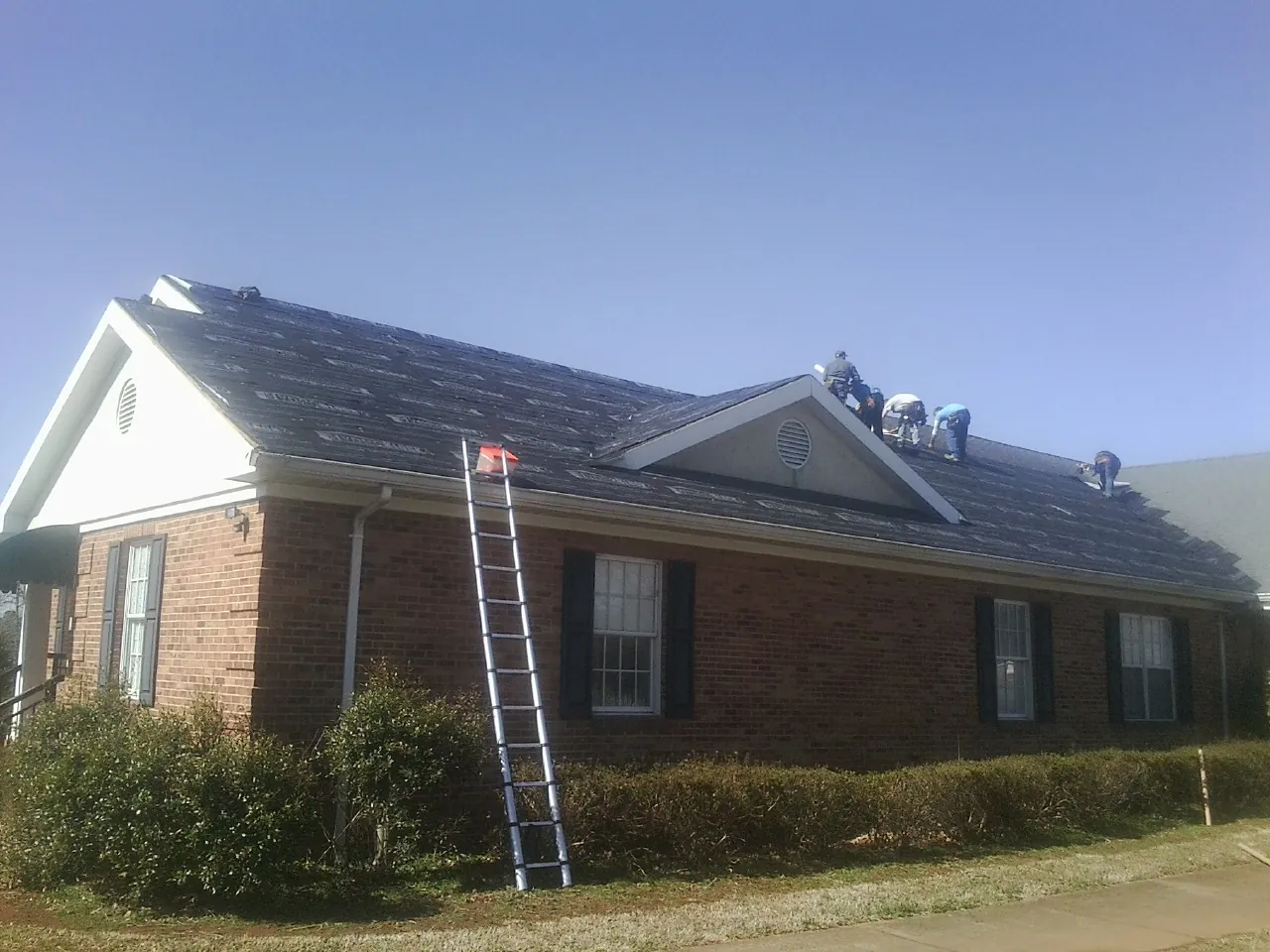 Crew tearing shingles off a brick ranch roof with a ladder set — Metal Roof Repair work by our crew in San Bruno