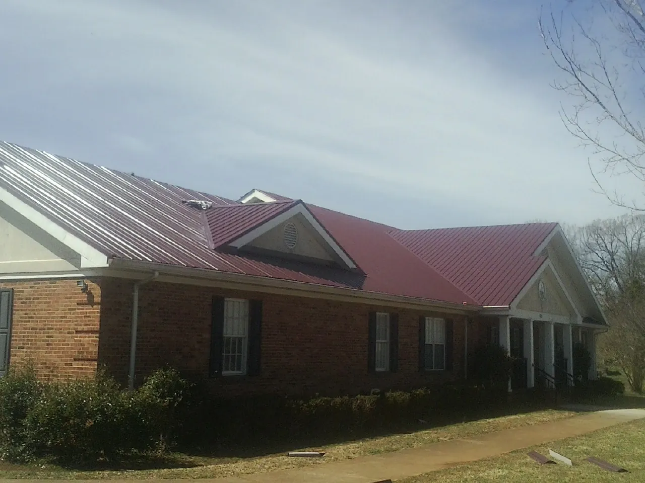 Red metal roof with gabled entries on a long brick building, from a Hail Damage Roof Repair job in San Bruno