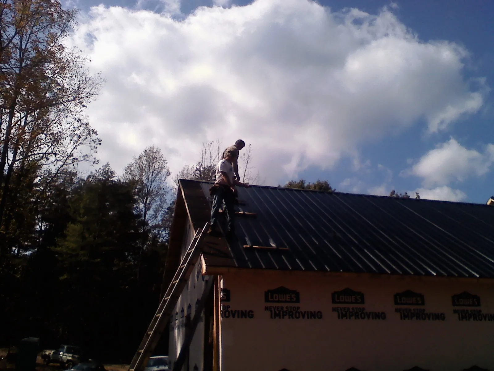 Roofer fastening dark metal panels high against a cloudy sky in San Bruno
