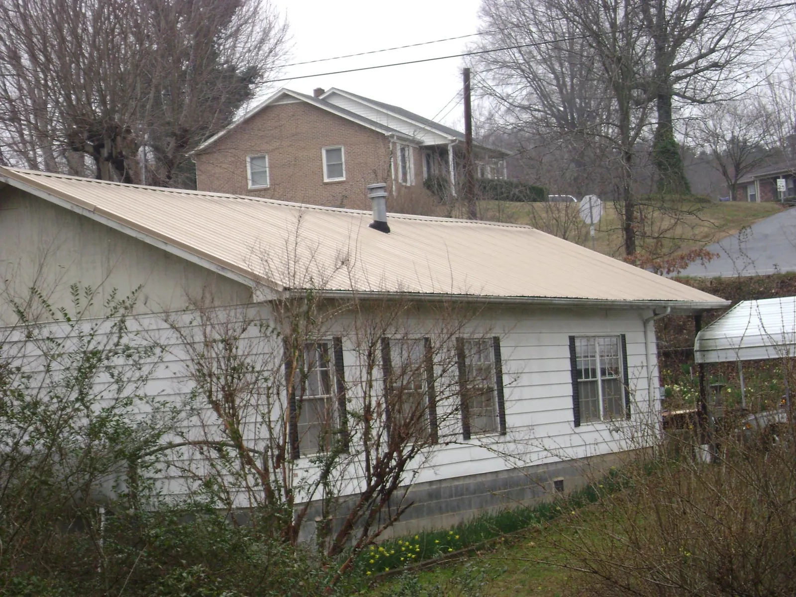 Tan metal roof on a white sided house set into a hillside — Commercial Roofing by Roofing Brothers in San Bruno